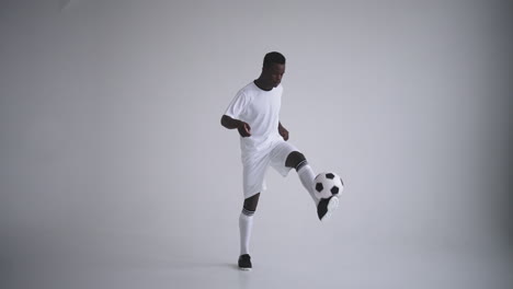 A-professional-black-football-player-in-a-white-uniform-on-a-white-background-juggles-a-ball-in-slow-motion.-African-American-ethnic-group-soccer-player-with-a-soccer-ball